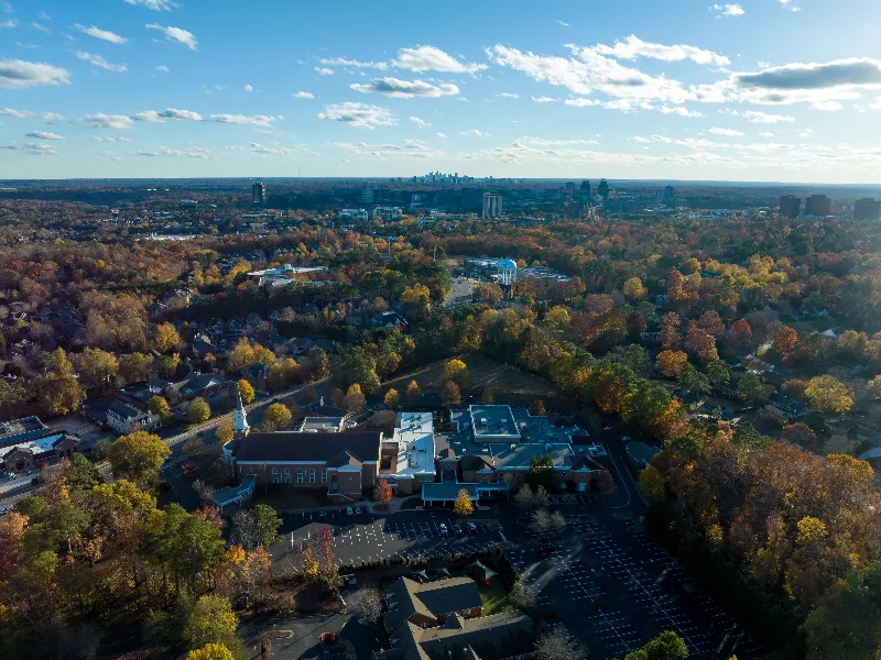Aerial view of a suburban area with autumn trees and a church with a steeple in the foreground.