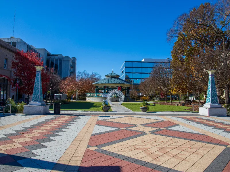 City park with a gazebo, decorative pillars, and autumn trees under a clear blue sky.