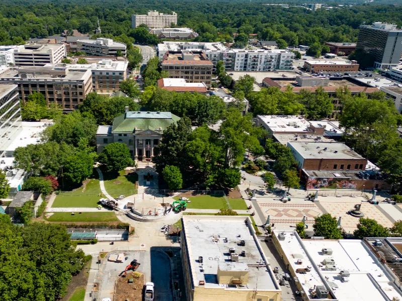 Aerial view of a city park with a historic building surrounded by trees and urban buildings.