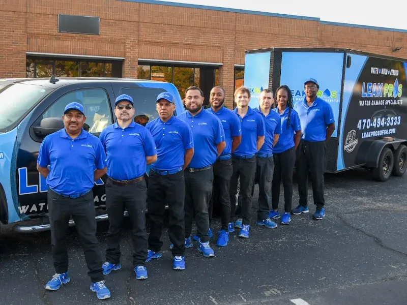 Eight uniformed workers stand in a line beside a branded truck and trailer for Leak Pros water damage specialists.