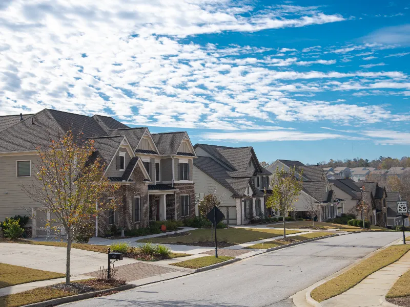 Suburban street lined with modern two-story houses under a partly cloudy sky.