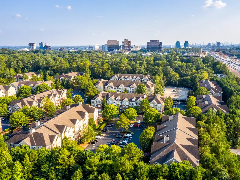 Aerial view of a residential apartment complex surrounded by trees with a city skyline in the background.