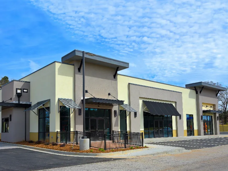 Newly constructed commercial building with large windows and black awnings under a blue sky.