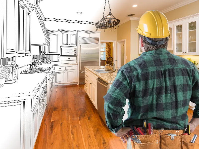Construction worker in a hard hat and tool belt stands in a partially sketched kitchen.