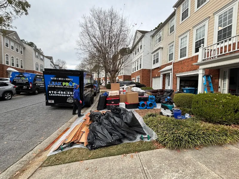 Trash bags, boxes, and cleaning equipment outside townhouses with a worker near a Leak Pro van.