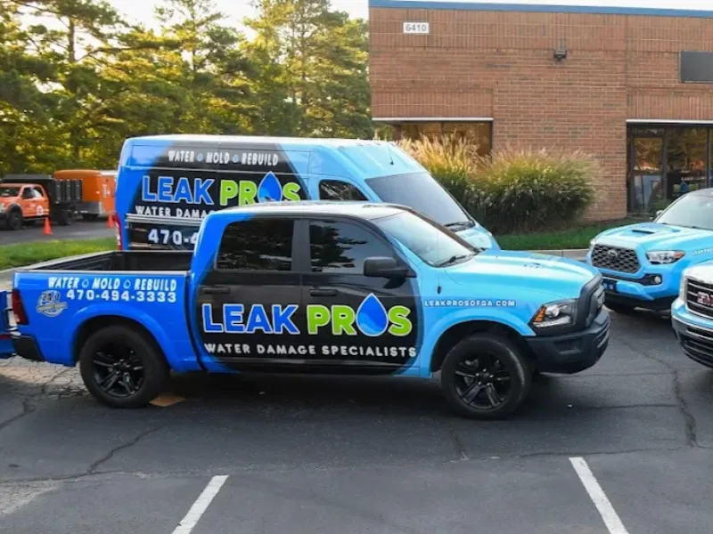 Blue and black Leak Pros water damage specialist truck and van parked outside a building.