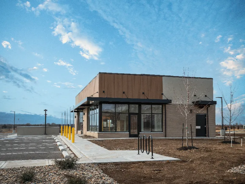 A small, modern commercial building with large windows and an empty parking lot under a partly cloudy sky.