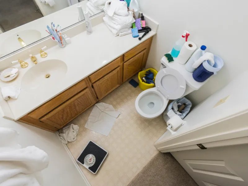 Small bathroom with a toilet, sink, wooden cabinet, and various toiletries and cleaning supplies.