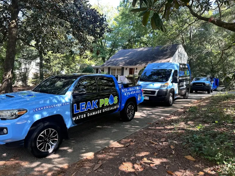 Three blue Leak Pros water damage specialist vehicles parked on a driveway in front of a house.